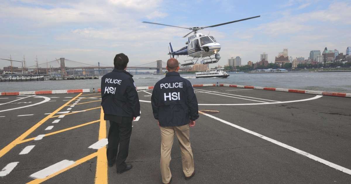 Two HSI agents watch a helicopter land. Photo credit: U.S. Customs & Immigration Enforcement, Flickr.com